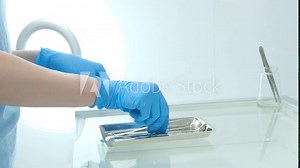 Hands in glove put the dental instruments on a little metal trays. Medical staff preparing tools for stomatology examination. Close up. High quality 4k footage
