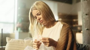 Nervous stressed woman popping bubble wrap trying to calm down sitting on sofa indoors Worried blond female bursts bubbles on packaging wrap at home Stress relief concept
