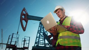 oil industry. engineer next to an oil rig. oil production business finance concept. gas production. a worker with a laptop monitors oil production next to an station. a worker sun in hard hat works