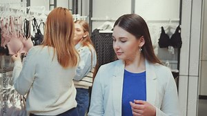 Three women shopping for lingerie, examining different bras and undergarments in store. Females focused on selecting items, showcasing variety of choices. Concept of fashion and retail therapy