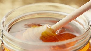 Honey dripping. Dipping honey with honey scoop in glass jar. Healthy organic food. Thick honey dripping from wooden spoon. Close-up in 4K, UHD