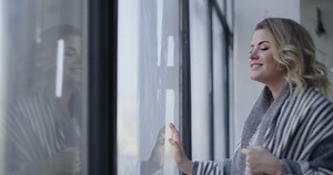 Attractive young woman comes to the big window and looks through it, watching somebody through the glass, checking the weather outdoors, waiting for somebody comming, 4k DCI 120 fps Prores HQ