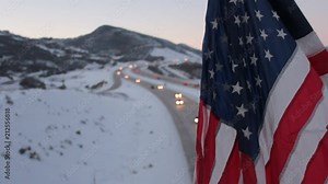 Old glory flying above a highway, as cars and trucks make there way.