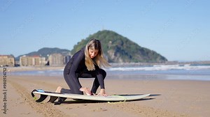 Young woman preparing the surfboard at the beach. Surfer applying wash to the board.