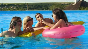 Pool party consisting of young people on inflatable ice cream rings relaxing in the pool at a luxury resort on summer vacation