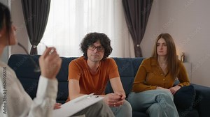 Young couple sits on couch in front of psychologist, discussing and working through their relationship problems. Professional help to overcome challenges in relationships