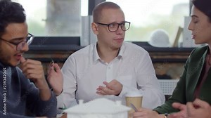 Professional male architect in eyeglasses and formal shirt explaining paper model of residential building to colleagues while discussing project in the office