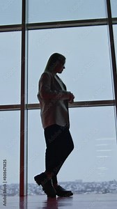 Woman in suit standing alone near the panoramic window. Long-haired lady watching the view and enjoying the cityscape. Vertical video