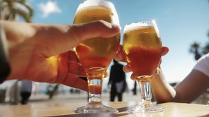 Friends drinking beer. People raising beer glasses to make a toast. Party outdoors on the beach during vacation.