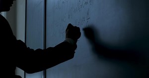 Scientist writing formulas on chalkboard. Hand with chalk wrote physics formulas on black chalkboard closeup