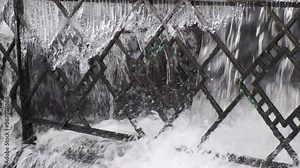 fragment of city park fence with frozen icicles with powerful river stream passing through, tracking camera movement
