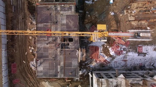 View of the construction of an apartment building from a height. The footage shows the activity of builders and heavy equipment. The boom of a large tower crane, metal structures and concrete
