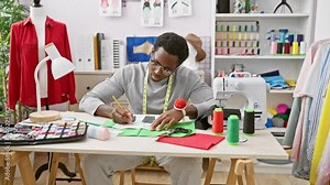 African man tailoring in a well-equipped atelier with red fabric on mannequin, sketching designs amidst colorful threads.