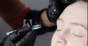 Hands of stylist in black gloves plucking eyebrows with tweezers. Beautiful woman doing correction eyebrow shape tweezing hairs.