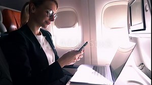 Young female entrepreneur sitting in business class seat during trip,working remotely on laptop computer connected to Wireless internet on board.Woman airplane passenger using mobile phone banking app