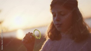 Young Girl Blowing Bubbles In Sunlight At Sunset