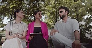 Three business colleagues having a casual meeting outdoors on a summer day. They're discussing a project while sitting on a bench.