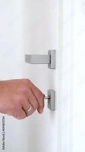 Man's hand inserting a key into a keyhole, turning it and opening a door