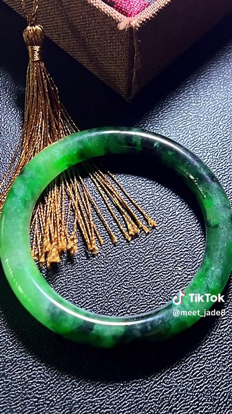 this jade bangle showcases a deeper, more intense shade of green, with darker and lighter hues blending beautifully throughout the piece. The rich, forest-like green transitions fluidly, with natural patterns and inclusions that add depth and character to the bangle. These darker, almost black-green sections provide a stunning contrast to the lighter, semi-translucent areas, making the bangle appear dynamic and full of life. The smooth, polished surface of the bangle enhances its natural beauty,