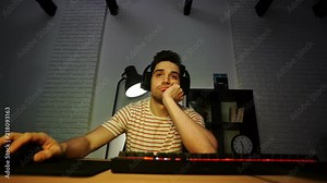 Bored brunette man in headphones sitting in front of computer and using it