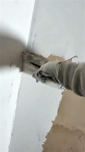 scraping off old white paint from a wall surface using a metal tool for renovation or cleaning