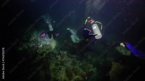 Group of scuba divers exploring deep dark ocean with flashlights