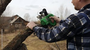Slow motion gardener using a electric circular saw makes a cut on an old apple tree trunk.