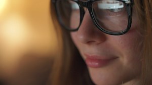 Woman in glasses looking on the monitor and surfing Internet at night. The monitor screen is reflected in the glasses. Work at night. Home Office. Remote work