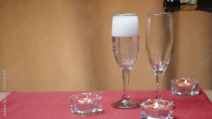 Romantic table for two. I pour champagne into two glasses. Candles on the red table.