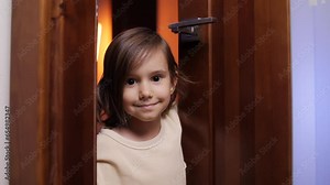 a little girl opens the door to the room and looks out from behind the door