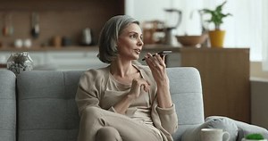 Middle-aged woman holds smartphone make call on speaker phone, send message or SMS in messenger using mobile voice recognition, browse information on internet with help of digital assistant. AI tech