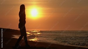 Full length woman in summer short dress, high lace-up boots walking on sandy beach at sunrise on summer morning. Silhouette female during weekend beach holiday at golden hour. Slow motion, handheld
