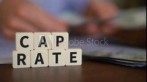 Concept of capitalization rate. Cape rate word with selective focus. Person counting cash on the background.