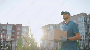 Blue delivery man send a package to customer on before deliver cargo. 4k resolution and slow motion shot. Male postman with parcel in hands at city street. Postal concept. Delivery service.