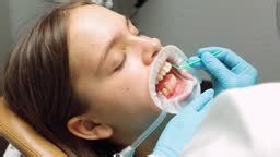 A dentist applies dental adhesive to a teenage patient's teeth using...