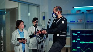 Team of medical researchers monitoring performance athlete with mask and electrodes attached on him measuring endurance, heart rate, psychological resistance, training muscle mass in science sport lab