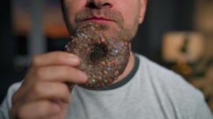 Man hastily eating sweet chocolate donut. Close-up