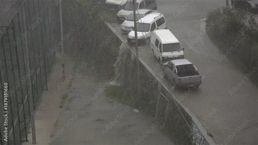 Extreme heavy rain pours through dense city streets, creating dramatic urban storm atmosphere. Torrential downpour floods roads and buildings, showing severe weather power and danger