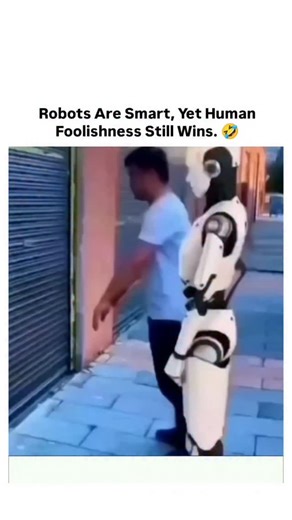 Laughing Zone on Instagram: "This 14-second clip captures a surprisingly funny moment between a human and a humanoid robot in an urban alleyway. A man wearing a blue shirt repeatedly nudges a white humanoid robot against a closed metal shutter. Each time, the robot tries to respond logically—awkwardly pushing back, recalculating its balance, and attempting to stay upright—before eventually stumbling away in confusion. The moment is captioned to highlight how human unpredictability can still outs