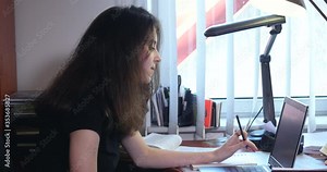 A close shot of cute and focused young girl using a laptop computer and writing on notebook, learning and doing homework sitting on the platform