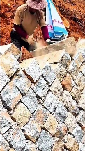 Worker arranging split stones to build a retaining wall using the stone masonry technique
