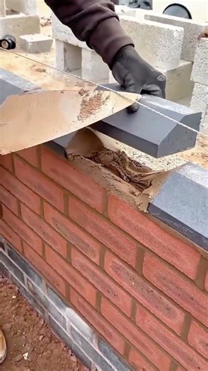 applying many black bricks on a red brick wall with a metal trowel in an outdoor garden area today