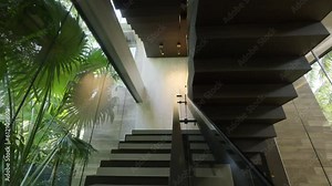 Dark concrete stairs with glass fencing inside luxury modern villa surrounded with green tropical plants. Contemporary interior design elements