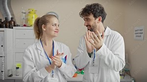 A woman and man in lab coats clapping hands joyfully in a well-equipped laboratory