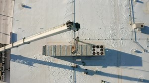 Aerial, crane tied to an industrial rooftop HVAC unit, installing onto building roof