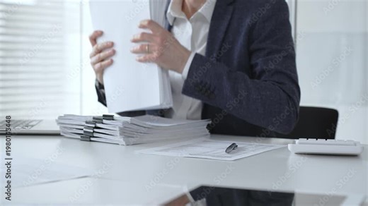 Business professional sorting a large stack of financial reports and tax forms with binder clips on a busy office desk. Audit and taxes
