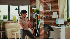 Female person singing and dancing in apartment, cleaning living room floors with mop and washing solution. Smiling housewife mopping tiles and having fun spring cleaning. Tripod shot.