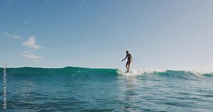 Young woman surfing a wave on her longboard, nose riding hanging ten on summer wave, happy longboarder
