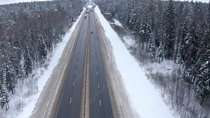 A blue car, rear view, drives forward right along the road in the middle of a forest covered with snow. A blue car drives along a highway among snow-covered trees and a roadside in a cold winter.