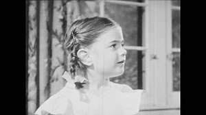 1950s: Little girl with braids watches her Mother kiss man at door. Woman and man holding briefcase stop hugging and kneel down to introduce man to little girl.
